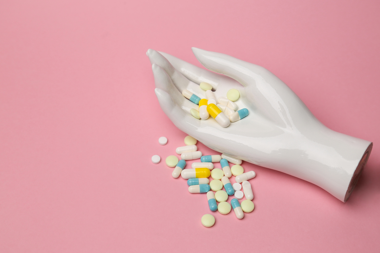 female mannequin hand on a pink background holding colorful pills. minimalism, place for text. the concept of fake medicines.