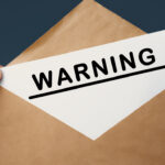 Male hand holding craft envelope with text WARNING on blue background